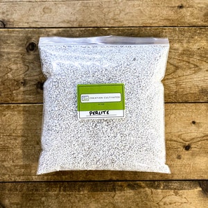 Puede incluir: Una bolsa blanca de perlita, un enmendante del suelo, con una etiqueta verde que dice "Creation Cultivated" y "Perlita".