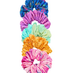 May include: Five patterned scrunchies in a vertical arrangement. The colours include blue, purple, teal, orange, and pink. Each scrunchie is made of fabric with a gathered, ruffled design. The background is plain white.