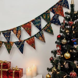 May include: A festive Christmas scene featuring a decorated tree with ornaments and lights, a patterned banner, and wrapped gifts. The banner has a repeating pattern of red, blue, and green. Three white candles are lit on a white surface.
