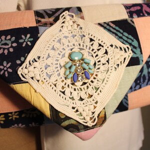 May include: A patchwork fabric clutch bag with a crocheted detail and a turquoise and blue jeweled embellishment.