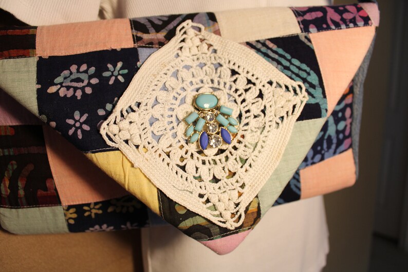 May include: A patchwork fabric clutch bag with a crocheted detail and a turquoise and blue jeweled embellishment.
