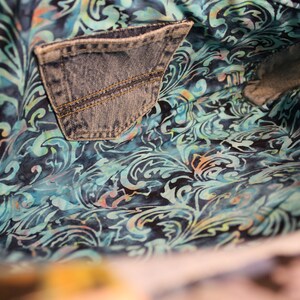 May include: The inside of a blue denim bag with a blue and teal floral pattern lining. The bag has a large pocket on the inside.