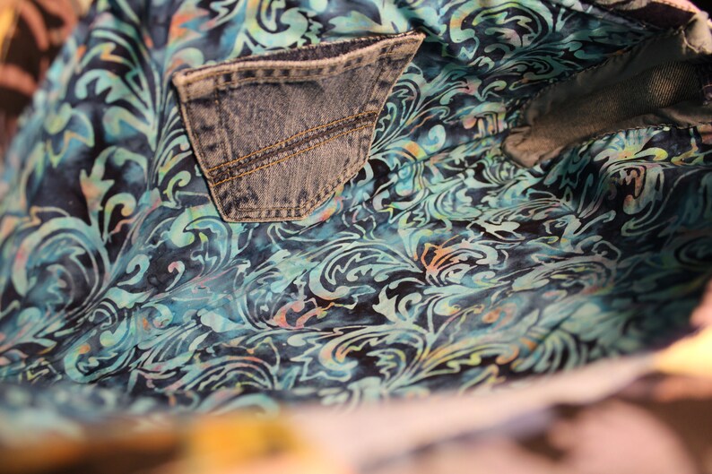 May include: The inside of a blue denim bag with a blue and teal floral pattern lining. The bag has a large pocket on the inside.