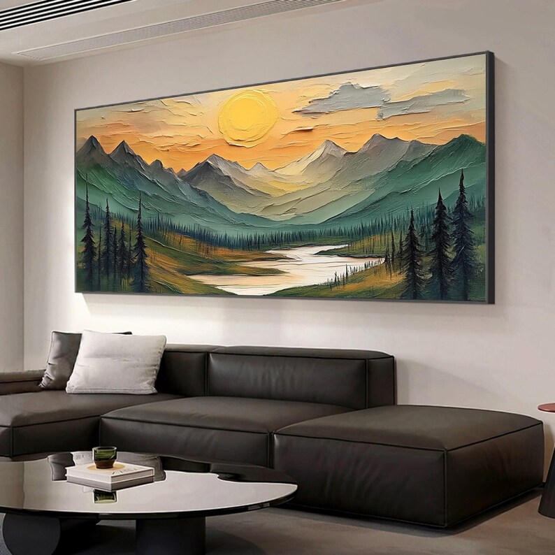 May include: A framed landscape painting depicts a mountain range under a yellow sun and a cloudy sky. The artwork features a river and trees in the foreground, with green and blue hues dominating the scene. The painting is displayed above a black leather sectional sofa.