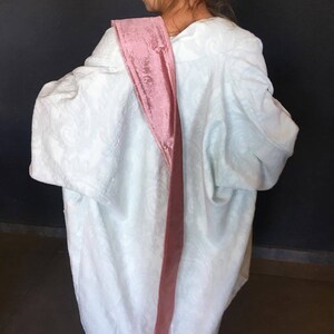 Pu&ograve; includere: Una veste bianca con una fascia di velluto rosa legata intorno alla spalla.
