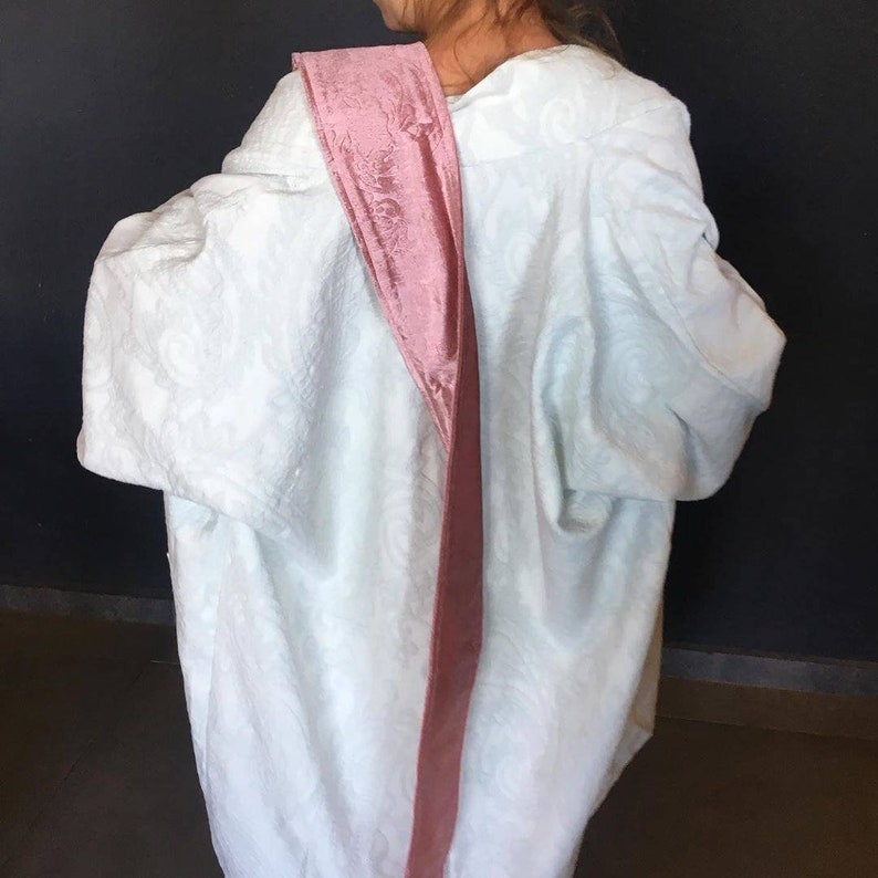 Pu&ograve; includere: Una veste bianca con una fascia di velluto rosa legata intorno alla spalla.