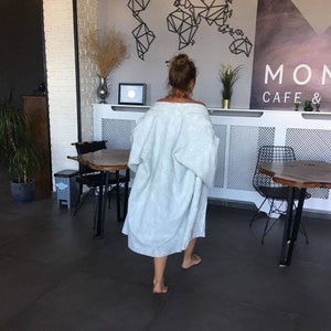 Pu&ograve; includere: Una persona che indossa una vestaglia blu chiaro cammina attraverso un caff&egrave; con le parole "MON CAFE &" sul muro.