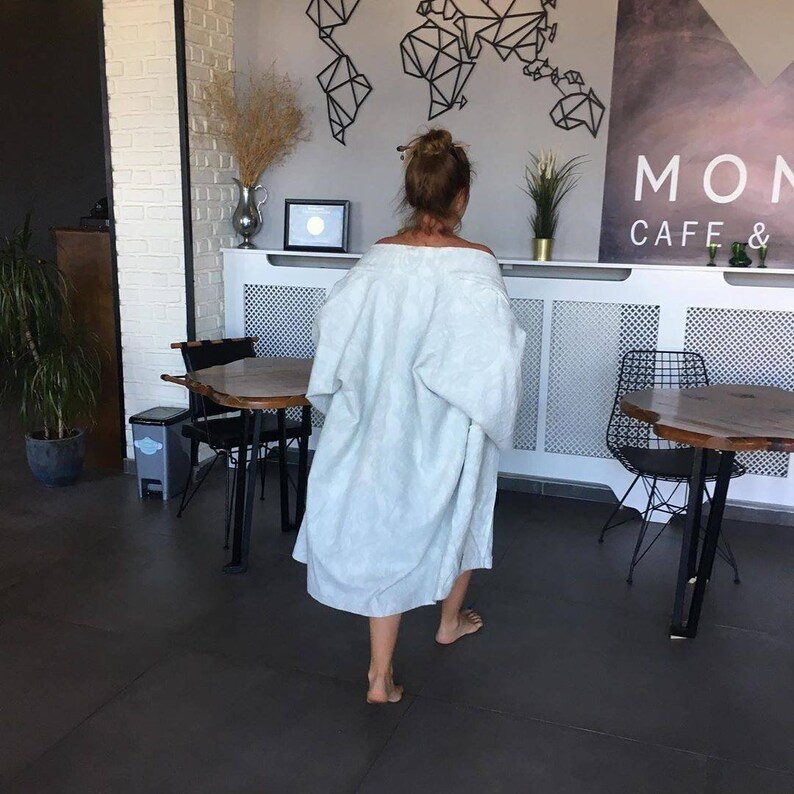 Pu&ograve; includere: Una persona che indossa una vestaglia blu chiaro cammina attraverso un caff&egrave; con le parole "MON CAFE &" sul muro.