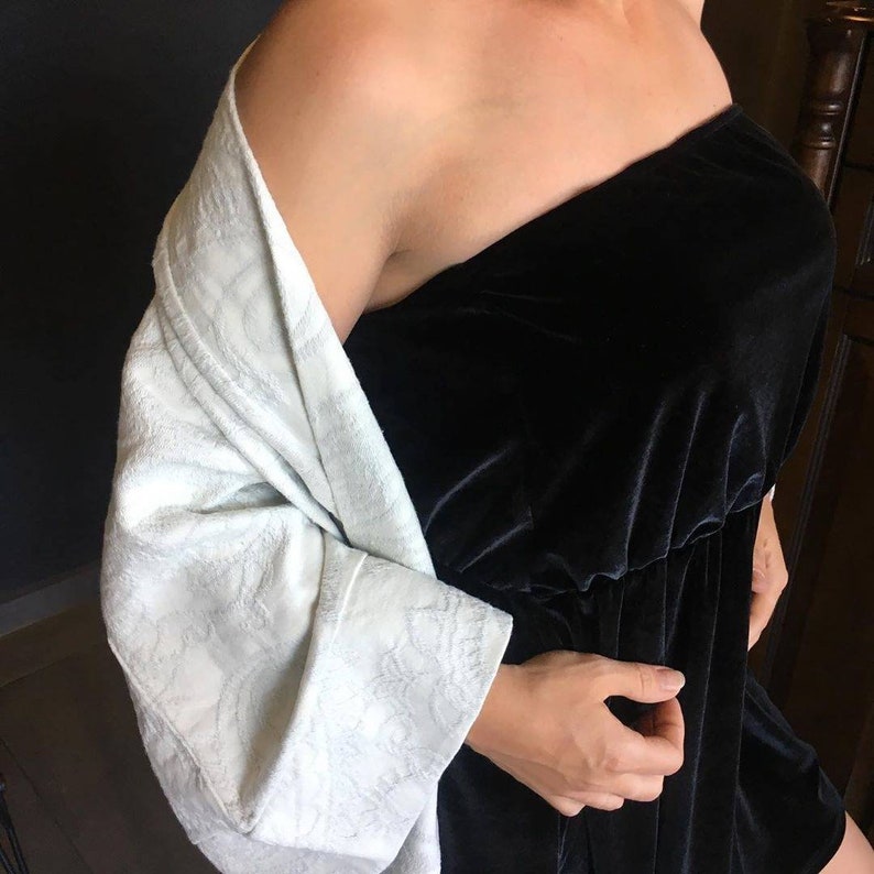 Pu&ograve; includere: Una veste bianca testurizzata in stile kimono con maniche lunghe e un abito nero in velluto senza spalline.