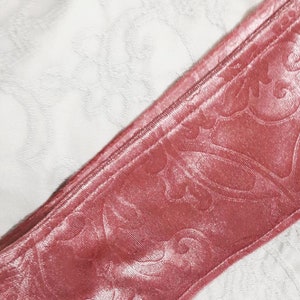 Pu&ograve; includere: Primo piano di un nastro di velluto rosa con un motivo floreale. Il nastro &egrave; piegato a met&agrave; e ha una texture liscia e setosa.