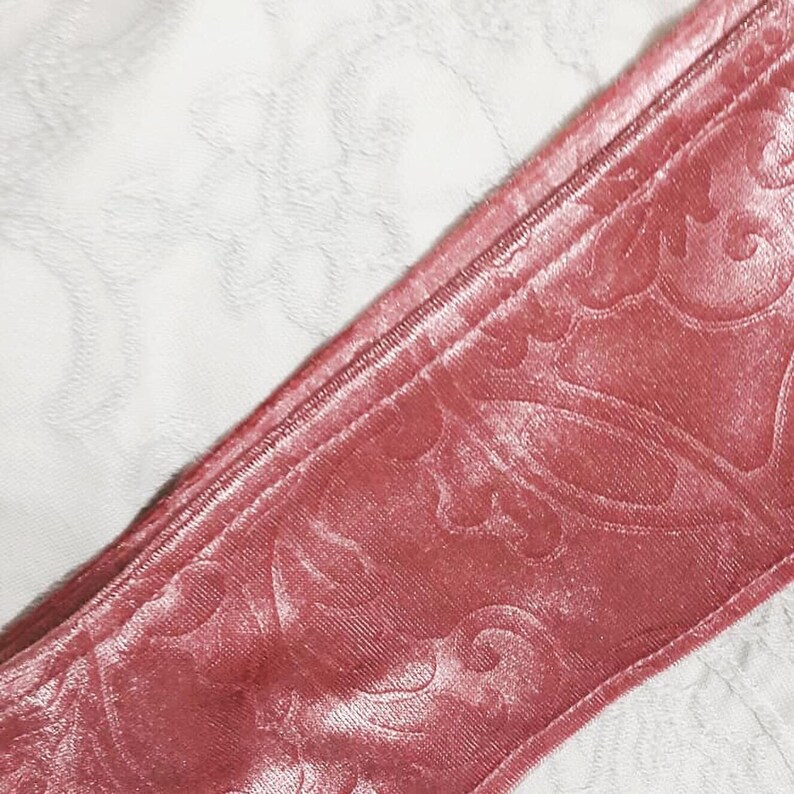 Pu&ograve; includere: Primo piano di un nastro di velluto rosa con un motivo floreale. Il nastro &egrave; piegato a met&agrave; e ha una texture liscia e setosa.