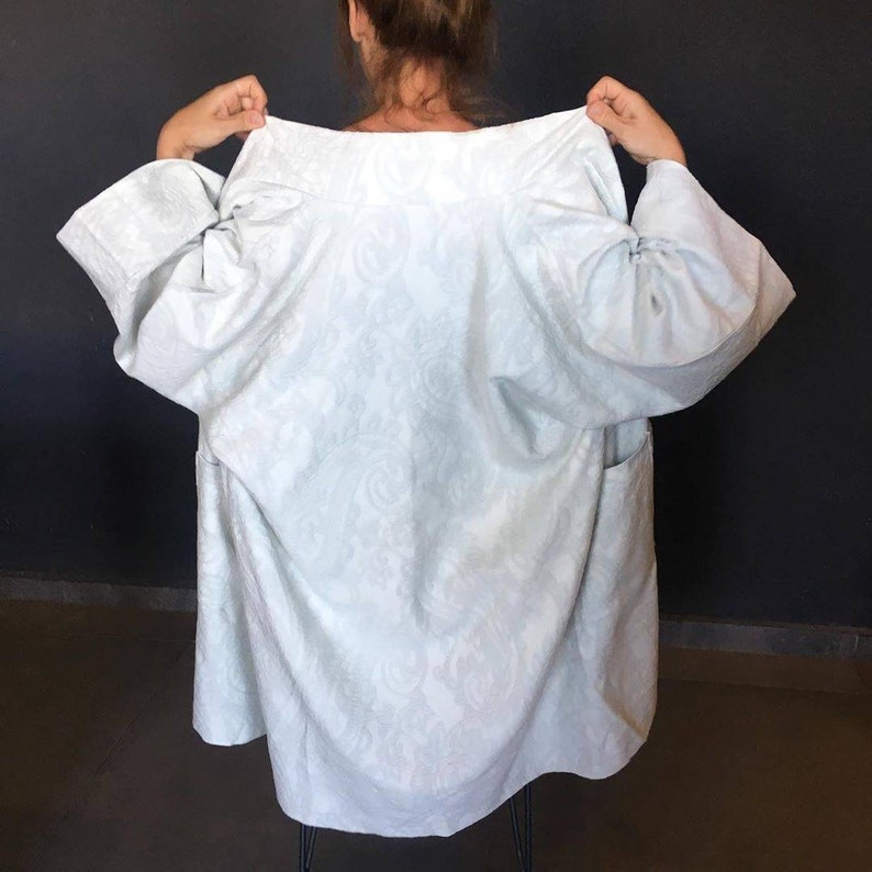 Pu&ograve; includere: Una giacca lunga a maniche lunghe di colore azzurro con un motivo floreale bianco. La giacca ha un colletto largo e una vestibilit&agrave; rilassata.