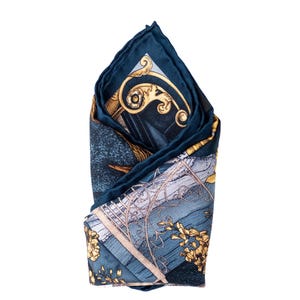 May include: A folded navy blue pocket square with a detailed design. The pocket square features gold floral and architectural elements on a blue background. The edges are a darker navy blue, creating a defined border.