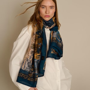 May include: A rectangular scarf featuring a deep blue base color with intricate, multi-colored floral and botanical patterns in shades of gold, brown, and cream. The lightweight fabric is draped around the neck, showcasing a detailed print design.