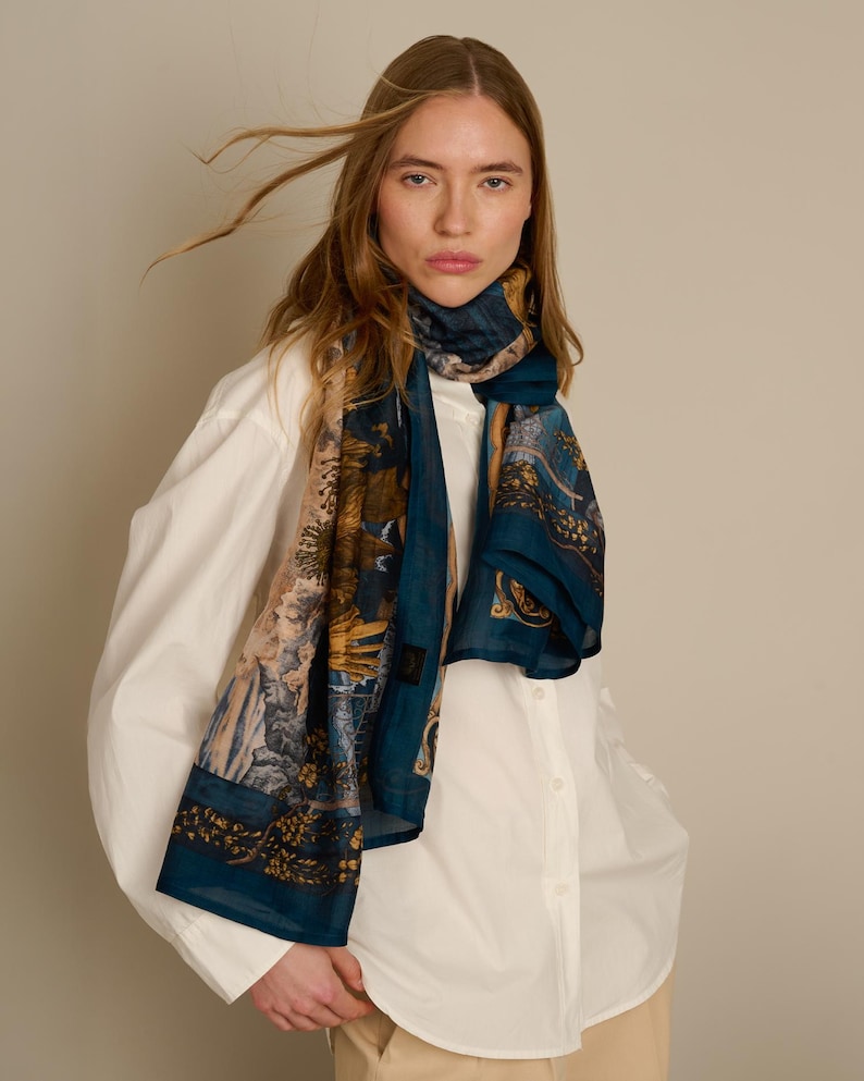 May include: A rectangular scarf featuring a deep blue base color with intricate, multi-colored floral and botanical patterns in shades of gold, brown, and cream. The lightweight fabric is draped around the neck, showcasing a detailed print design.