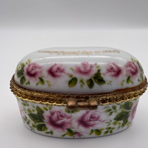 May include: White porcelain trinket box with a gold trim and a hinged lid. The box is decorated with pink roses and green leaves. The lid has the words "Great is thy faithfulness" written in gold lettering.