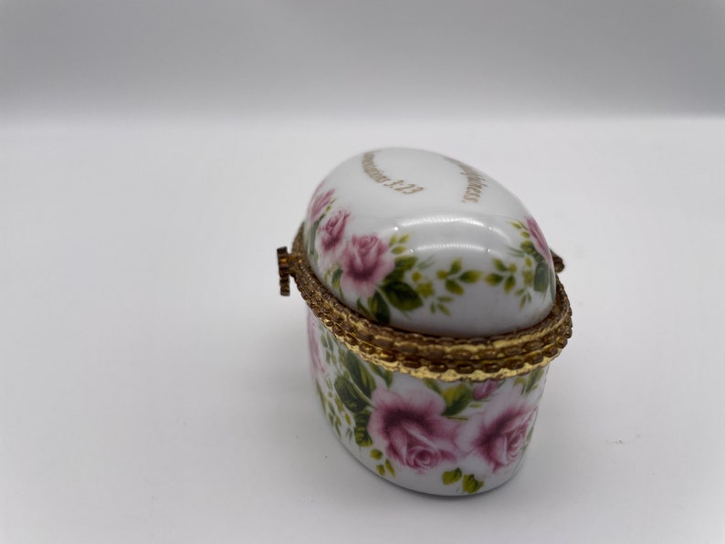 May include: Oval porcelain trinket box with a gold trim and floral design. The box is decorated with pink roses and green leaves. The lid has the inscription "Remember Me" in gold lettering.
