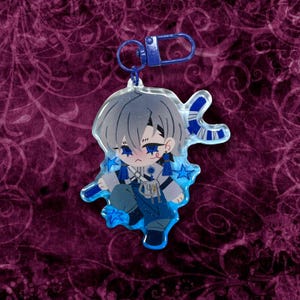 May include: A clear acrylic charm featuring a chibi anime character with gray hair and blue accents. The charm has a blue clasp and is decorated with blue stars. The character is wearing a blue and white outfit.
