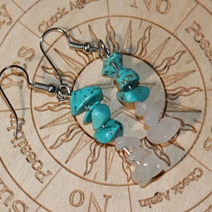 May include: A pair of dangle earrings featuring silver-toned metal hooks. Each earring is composed of three irregular, tumbled turquoise-colored stone chips followed by three irregular, tumbled pale pink stone chips arranged in a vertical line.