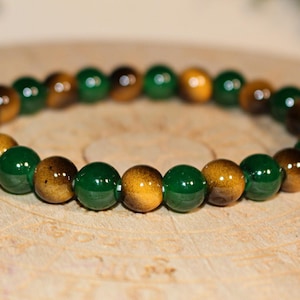 May include: A stretch bracelet composed of alternating round beads in polished forest green and golden brown tiger eye. The beads are arranged in a repeating pattern, creating a circular band with a smooth, reflective finish on each individual stone.