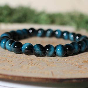 May include: A stretch bracelet composed of smooth, round beads in alternating shades of deep blue and black. The beads feature a polished, reflective surface with a subtle chatoyant luster, creating a consistent circular pattern around the wrist accessory.