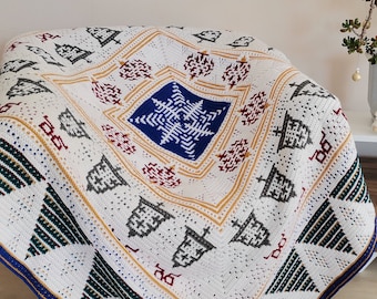 May include: A white crocheted throw blanket with a blue snowflake design in the center. The blanket has a geometric pattern of green, yellow, and red accents.