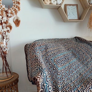 May include: A brown, blue, and white crocheted throw blanket with a geometric pattern. The blanket is folded and draped over a couch.
