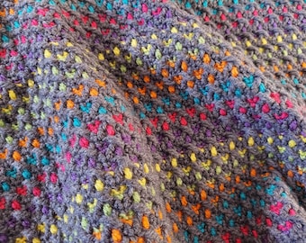 May include: A close-up of a grey crocheted blanket with colourful stripes of orange, yellow, green, blue and pink.