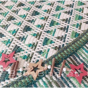 Può includere: Una coperta all'uncinetto fatta a mano nei toni del bianco, verde e verde acqua, con un motivo strutturato. La coperta è decorata con ornamenti a forma di stella in legno e bastoncini di cannella. Il testo "Beba Blanket" è visibile.