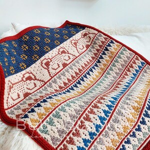 May include: A crocheted blanket with a geometric pattern in shades of red, blue, yellow, and white. The blanket has a red border and a textured design.