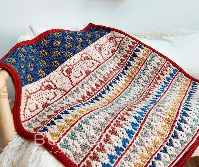 May include: A crocheted blanket with a geometric pattern in shades of red, blue, yellow, and white. The blanket has a red border and a textured design.