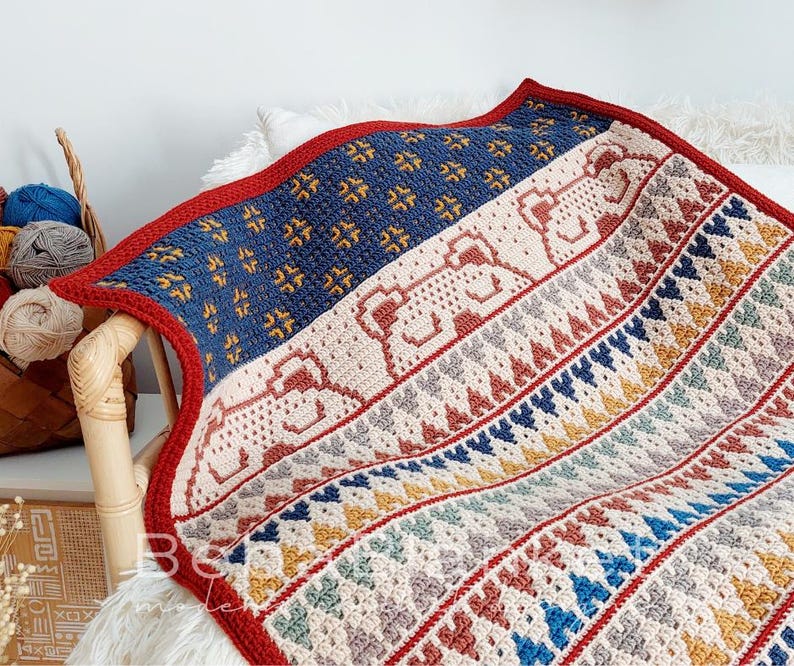 May include: A crocheted blanket with a geometric pattern in shades of red, blue, yellow, and white. The blanket features a repeating pattern of stylized animal figures.