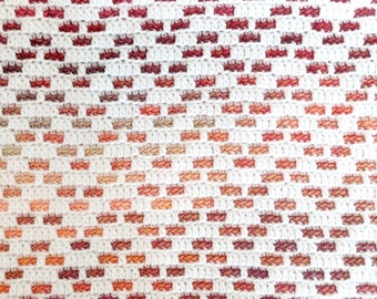 May include: A white crocheted blanket with a gradient pattern of red, orange, and brown squares.