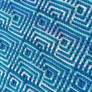 Puede incluir: Una manta de ganchillo azul, verde y blanca con un patrón geométrico.