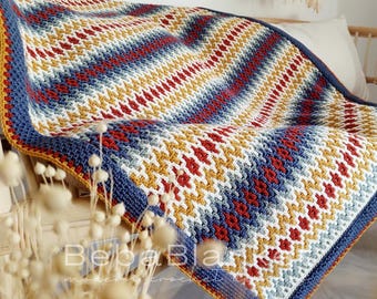 May include: A handmade crochet blanket with a geometric pattern in red, white, blue, and yellow. The blanket has a blue border with a yellow trim. The blanket is draped over a wooden frame.