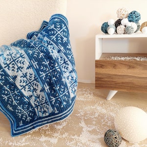 May include: A blue and white patterned blanket draped over a cream-coloured chair. The blanket features a geometric design in shades of blue and white. Decorative spheres in various colours and textures sit on a white side table.
