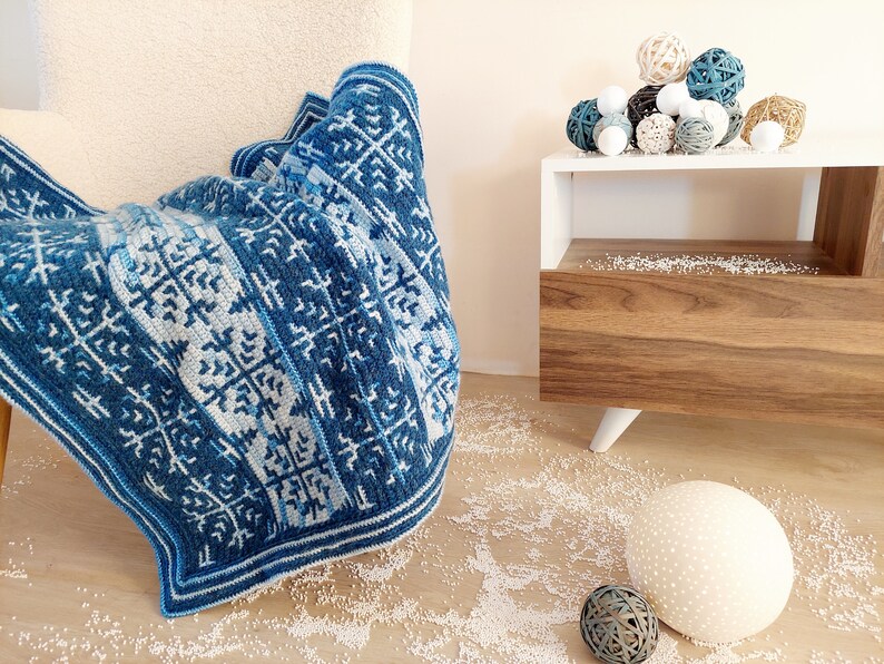 May include: A blue and white patterned blanket draped over a cream-coloured chair. The blanket features a geometric design in shades of blue and white. Decorative spheres in various colours and textures sit on a white side table.