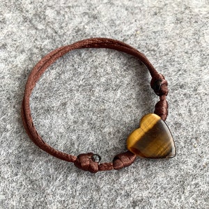 Könnte beinhalten: Ein braunes Kordel-Armband mit einem herzförmigen Tigerauge-Edelstein.