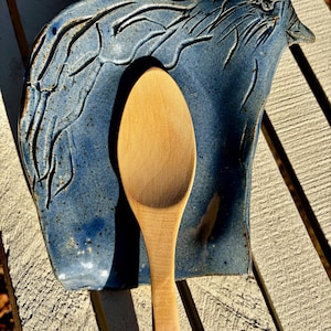 May include: A blue ceramic spoon rest shaped like a bird with a wooden spoon resting inside.