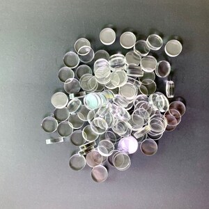 May include: A large pile of clear glass circles, some with a slight iridescent sheen, on a gray background.