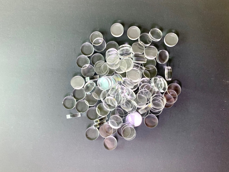 May include: A large pile of clear glass circles, some with a slight iridescent sheen, on a gray background.