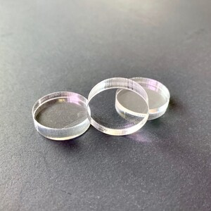 May include: Three clear acrylic circles stacked on top of each other. The circles are smooth and have a slight shine.