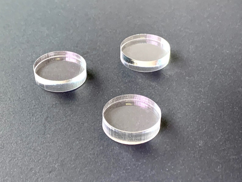 May include: Three clear acrylic circles, each with a slightly different diameter, are arranged on a dark gray surface.