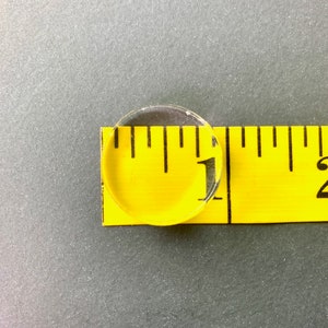 May include: A clear plastic circle measuring 1 inch in diameter on a yellow measuring tape with black markings. The tape reads "1" and "2".