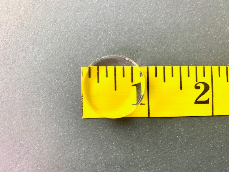 May include: A clear plastic circle measuring 1 inch in diameter on a yellow measuring tape with black markings. The tape reads "1" and "2".