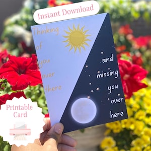 May include: A printable card with a split design featuring a sun and moon. The left side has a yellow sun and the words "Thinking of you over there." The right side has a moon, stars, and the words "and missing you over here."