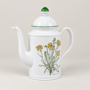 May include: A white porcelain coffee pot featuring a green-topped lid and a botanical illustration of yellow flowers with green leaves on the front. The vessel has a curved handle and a long, elegant spout, with a small green line accent.