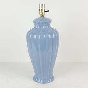 May include: A light blue ceramic table lamp with a ribbed design. The lamp has a brass-colored socket and a black on/off switch. The lamp is approximately 18 inches tall.