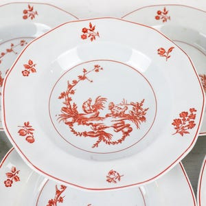 May include: A collection of white ceramic plates with a red floral and rooster design. The plates have a scalloped edge and a red border. The central design features a rooster and other decorative elements. Ideal for serving food.