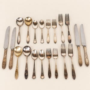 May include: A collection of twenty pieces of vintage silver-plated flatware arranged in two rows. The set includes four dinner knives, four large spoons, four small spoons, four dinner forks, and four salad forks, all featuring ornate floral handles.